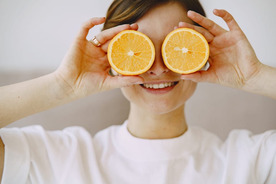 Woman hold slices of orange over her eyes.