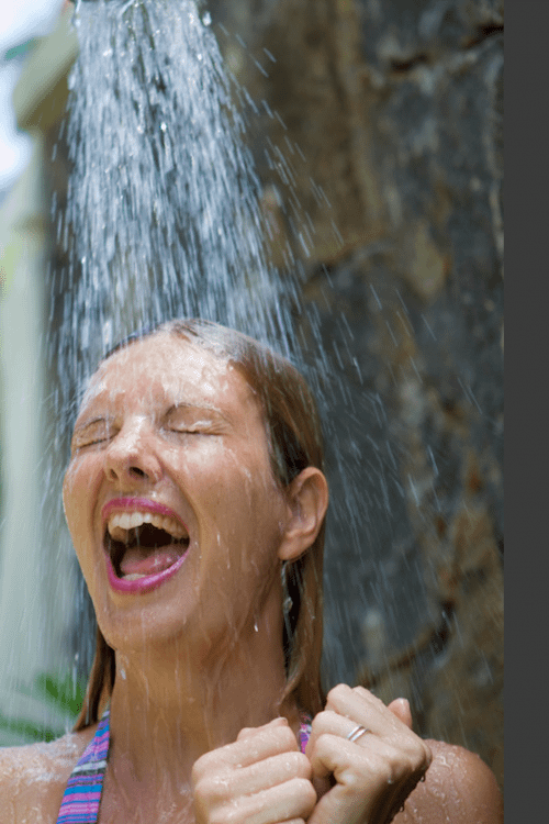 A young woman taking a cold outdoor shower to showcase the mental health benefits of cold showers