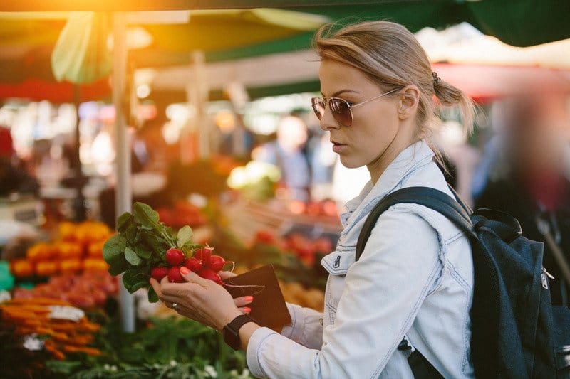 a shopping examines produce at farmers market. This image illustrates the importance of shopping smart at farmers markets to get the most for your money.
