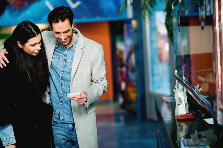 Happy couple buying movie tickets at the cinema - used as an example to illustrate a type of illogical thinking: Mental Accounting Behavior that can affect our money sense