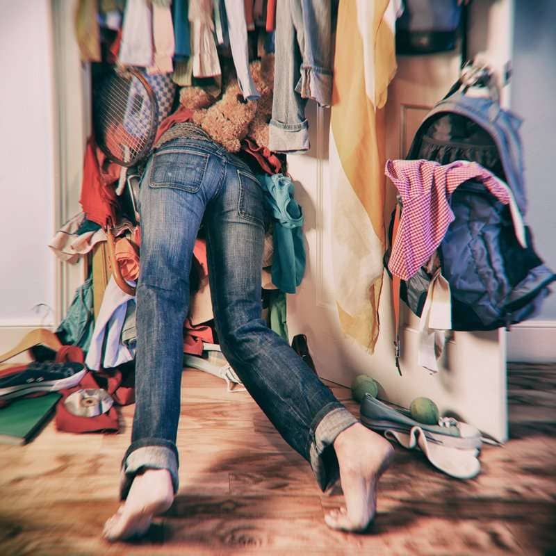 the image of a woman searching in a messy closet to illustrate the physical and mental benefits of decluttering