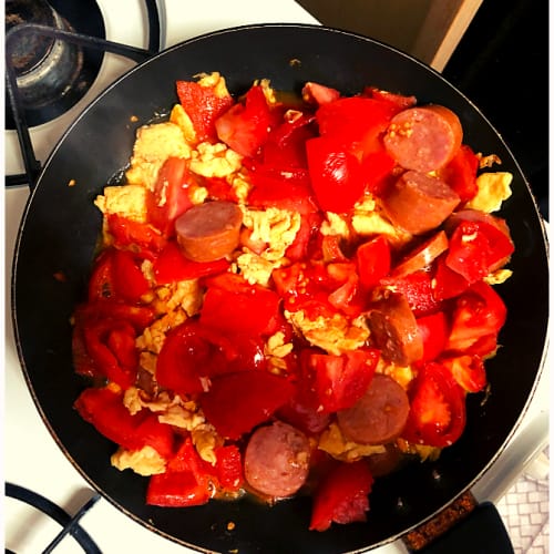 a cooking pan on stove containing scrambled eggs, freshly sliced tomatoes, and sausage. This image illustrates how fresh and inexpensive produce can be at farmers market.