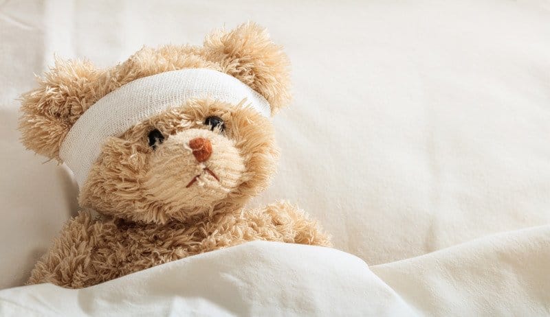 This is an image of a teddy bear sick in bed, which shows the concept of someone who is sick and bedridden.