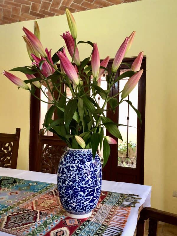 a bunch of pink lilies in a blue vase atop a Mexican-styled dining table.